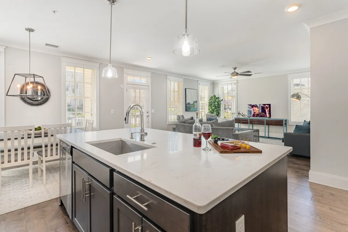 A wide-angle view of an open-concept living space that seamlessly connects the kitchen island, dining area, and living room seating. A large smart TV is mounted on the wall, and the area is set up for entertaining and relaxation with comfortable sofas and a warm, inviting atmosphere.