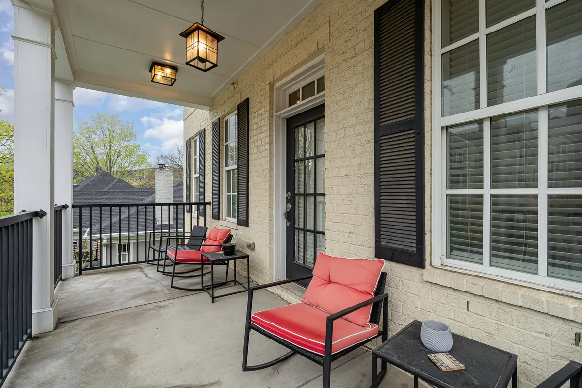 An exterior view of a porch area with red chairs, black railing, and a welcoming doorway, ideal for relaxing after a day out. The scene feels comfortable and inviting, suitable for family or pet-friendly moments.