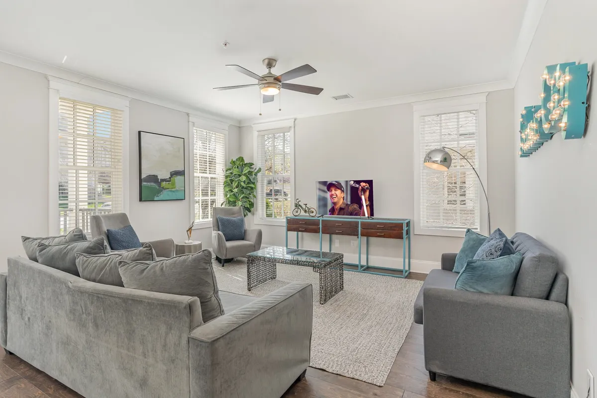The image showcases a stylish, inviting living room with a plush sofa, chic coffee table, vibrant artwork, lush plant, and a large television. The room exudes a cozy atmosphere, perfect for relaxing, entertaining guests, or gathering for a movie night.