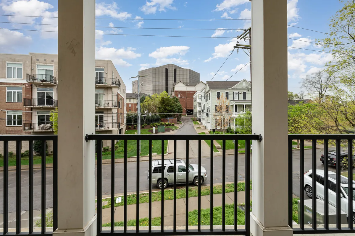 A private balcony overlooks a scenic neighborhood street, bordered by surrounding buildings. The view suggests a calm retreat above the lively city, ideal for unwinding or socializing after a night out.
