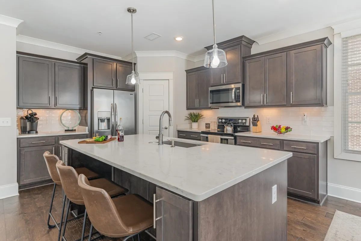 A modern kitchen with a spacious island, stainless steel appliances, pendant lighting, and decorative plants. The island offers ample space for meal prep, baking with kids, or casual dining, making it a natural hub for social interaction.