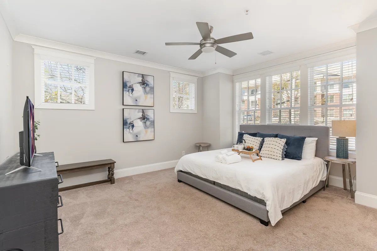 A tranquil bedroom featuring a neatly made bed with soft linens, elegant artwork on the walls, large windows allowing natural light to filter in, and a cozy bedside lamp. The space exudes calm and comfort, inviting restful sleep and relaxation.