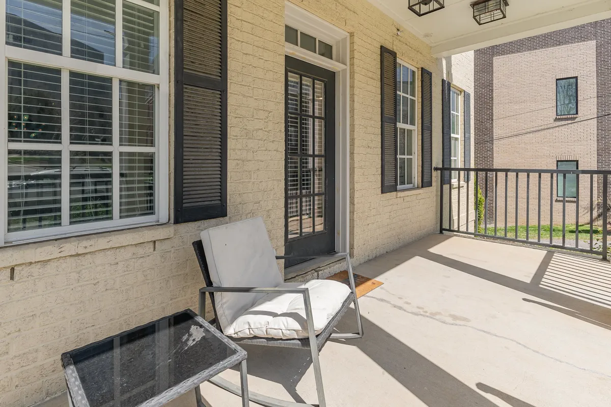 This image features an exterior view of a private porch or balcony area, complete with a comfortable chair and table positioned next to a doorway. The atmosphere is calm, inviting, and ideal for relaxing, reading, or enjoying a cup of coffee while soaking in the fresh air.
