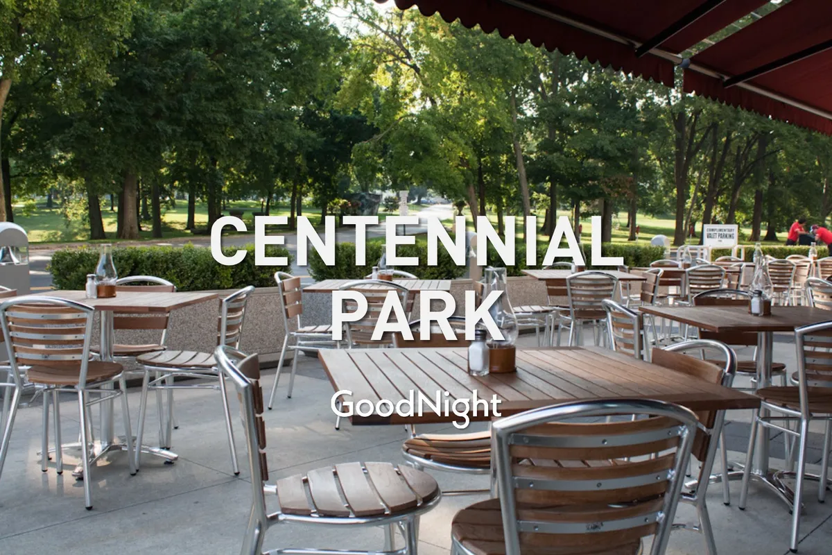 An exterior scene of an outdoor communal area, featuring tables and chairs underneath a canopy amidst lush greenery. The mood is cheerful and social, suggesting opportunities for outdoor dining, social gatherings, and community events.
