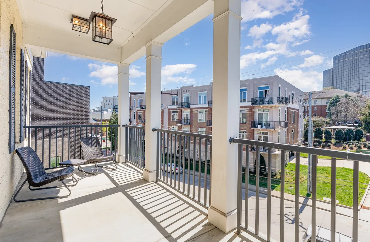 A tranquil private balcony with a modern railing, comfortable seating area, and a hanging light fixture. The scene is elevated, hinting at expansive city views beyond the balcony, ideal for unwinding or socializing as the day ends.